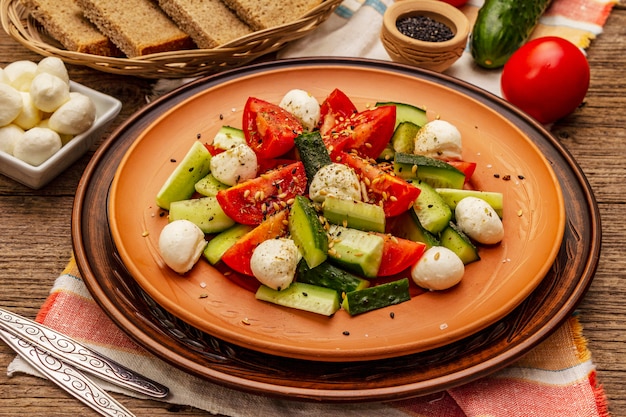 Frischer Salat aus Tomaten, Gurken und Babymozzarella. Sonniges Mittagessen mit knusprigem Brot