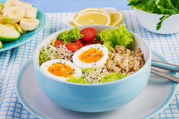 Frischer Salat. Frühstücksschüssel mit Haferflocken, Tomaten, Salat, Microgreens und gekochtem Ei.