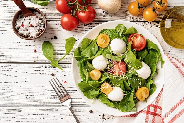 Frischer Salat mit Arugula-Kirschtomaten-Mozzarella-Käse und Hartkäse auf weißem Holzhintergrund Draufsicht