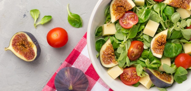 Frischer Salat mit Feigen, grünen Blättern, Kirschtomaten und Käse auf Grau