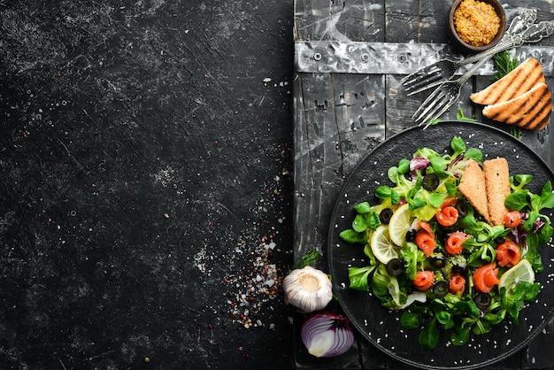 Frischer Salat mit Lachs und Oliven in schwarzer Platte Draufsicht Freier Platz für Ihren Text Rustikaler Stil