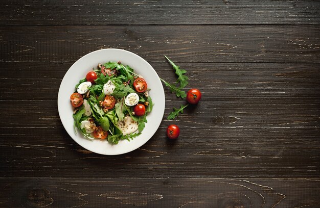 Frischer Salat mit Tomaten, gemischtem Grün, Nüssen, Eiern, auf hölzernem Hintergrund. Gesundes Essen.