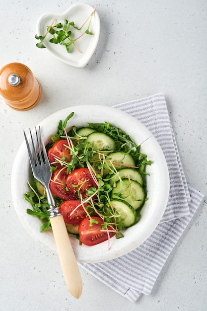 Frischer Salat mit Tomaten, Gurken, Gemüse, mikrogrünen Radieschen in weißer Platte auf grauem Stein