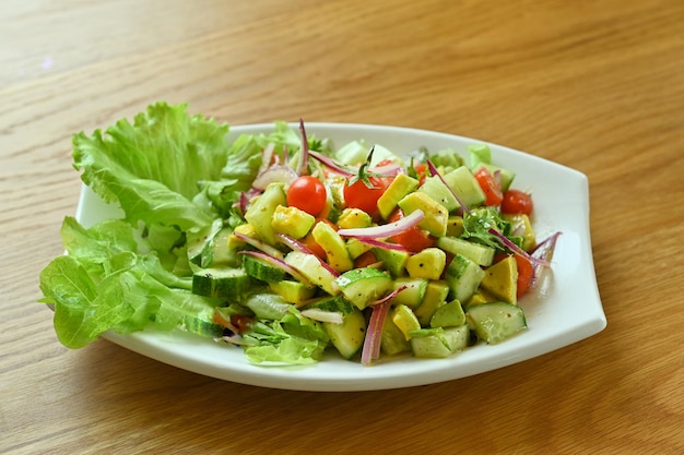 Frischer Salat-Tomaten-Avocado-Zitrone mit Olivenöl in weißer Schüssel auf Holztisch