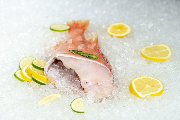 frischer Seeozean-Rotbarschfisch, auf Eis liegend, kopflos, Kirsche, in Scheiben geschnittene Zitrone und in Scheiben geschnittene Limette,