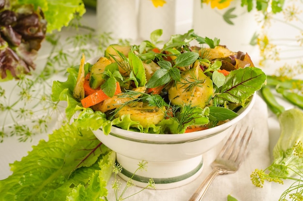 Frischer Sommersalat mit Zucchini-Karotten und Kräutern in einer Schüssel auf einem hellen Holztisch