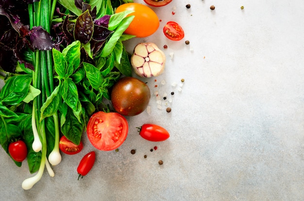 Frischer Spinat, Frühlingszwiebel, Basilikum, Kräuter, Dill und Tomaten auf grauem konkretem Hintergrund, selektiver Fokus.