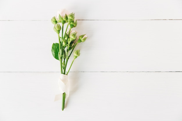 Frischer Strauß kleiner rosa Rosen mit Knospen mit weißem Band. Minimalistische flache Lage, weißer Holzhintergrund.