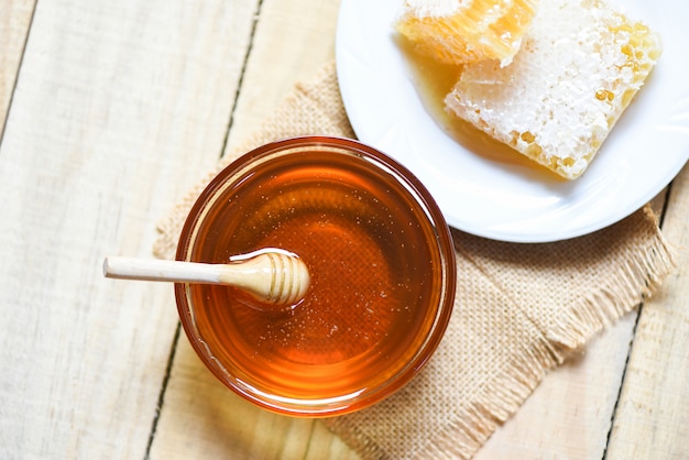 Frischer süßer Honig im Glas mit hölzernem Schöpflöffel und Bienenwabe auf Platte auf hölzerner Tabelle