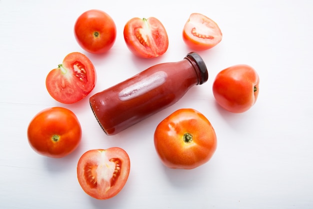 Frischer Tomatensaft in den Flaschen- und frischen Tomatenscheiben auf weißem hölzernem Hintergrund.