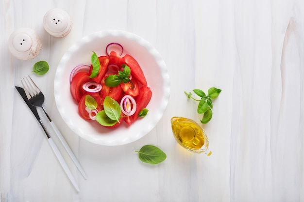 Frischer tomatensalat mit basilikumblättern, olivenöl und zwiebeln in weißer schüssel auf hellem hintergrund traditionelle italienische oder mediterrane ernährung draufsicht