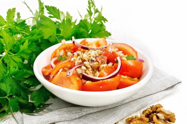 Frischer Tomatensalat mit Walnüssen und roten Zwiebeln, gewürzt mit Olivenölessig Bockshornklee und Salz in einem Teller auf einem Handtuch auf einem Hintergrund aus hellem Holzbrett