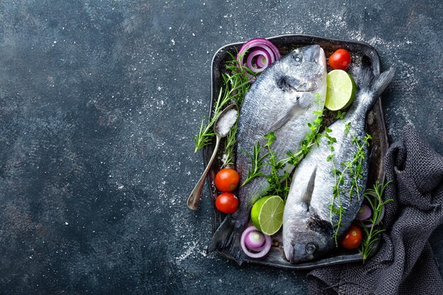 Frischer, ungekühlter Dorado-Fisch oder Seebräume mit Zutaten zum Kochen auf dunklem Hintergrund, Top-View