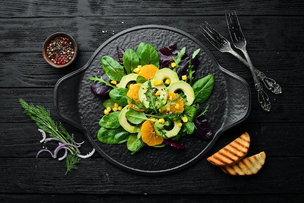 Frischer veganer Avocadosalat mit Orangen und Spinat auf einem schwarzen Teller Rustikaler Stil Draufsicht Freier Platz für Ihren Text