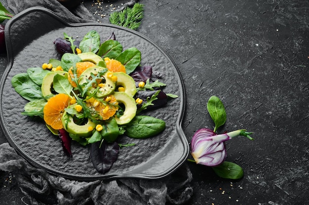 Frischer veganer Avocadosalat mit Orangen und Spinat auf einem schwarzen Teller Rustikaler Stil Draufsicht Freier Platz für Ihren Text