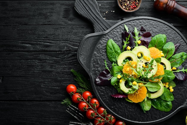 Frischer veganer Avocadosalat mit Orangen und Spinat auf einem schwarzen Teller Rustikaler Stil Draufsicht Freier Platz für Ihren Text