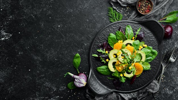 Frischer veganer Avocadosalat mit Orangen und Spinat auf einem schwarzen Teller Rustikaler Stil Draufsicht Freier Platz für Ihren Text