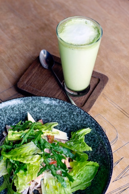 Frischer vegetarischer Salat und Matcha Latte auf einem Holztisch.