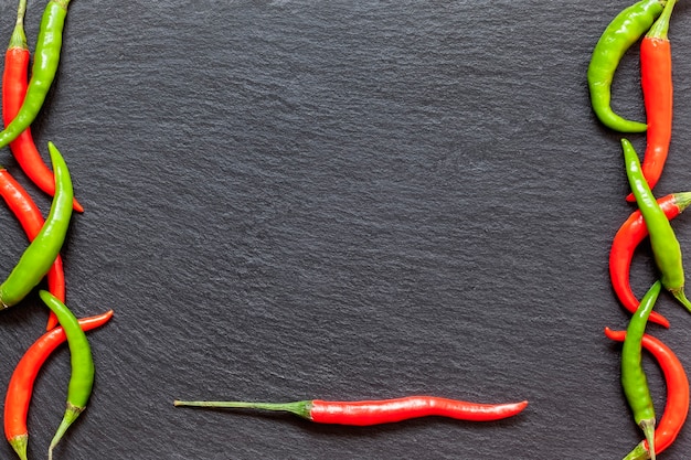 Frischer würziger roter und grüner Pfeffer auf einem Schieferbrett, verschiedene bunte Chilischoten und Cayennepfeffer auf dunklem Hintergrund von oben. Draufsicht, Kopierraum.