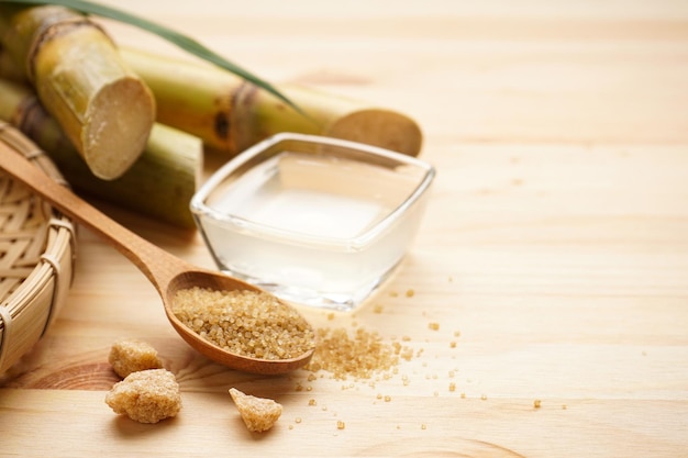 Frischer Zuckerrohrsaft und brauner Zucker auf einem hölzernen Hintergrundraum für Text