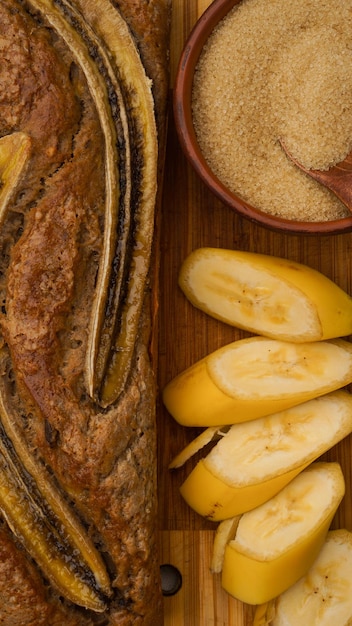 frisches Bananenbrot, umgeben von frischen Bananen und Kochzutaten, liegt auf grauem Hintergrund