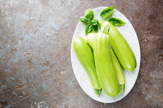 Frisches Bio-Sommergemüse-Zucchini auf einem Teller auf rustikalem grauem Steinhintergrund. Ansicht von oben, Platz für Text.