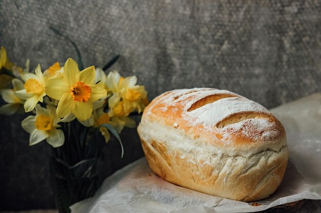 Frisches Brot nur aus dem Ofen kühlt auf Pergamentpapier in der Nähe von schönen Blumen ab