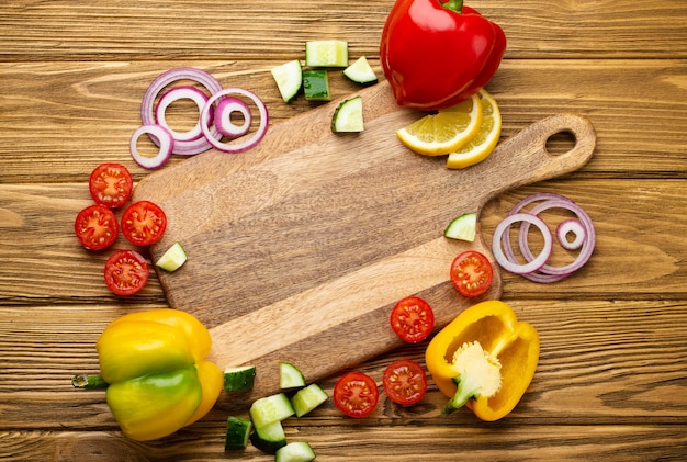 Frisches buntes Gemüse und gesunde Kochzutaten um leeres Schneidebrett, rustikaler Holzhintergrund. Zutaten für die Herstellung von Salat oder gesunde Mahlzeit. Diät halten, kochen, sauber essen, Platz kopieren