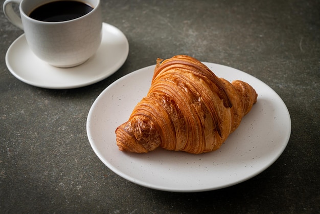 frisches Croissant auf weißem Teller mit schwarzem Kaffee