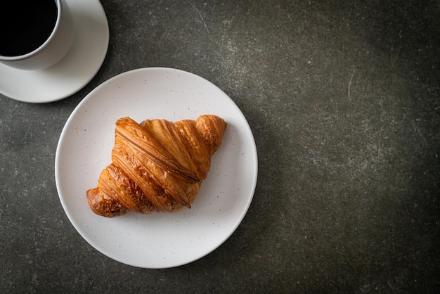 frisches Croissant auf weißem Teller mit schwarzem Kaffee