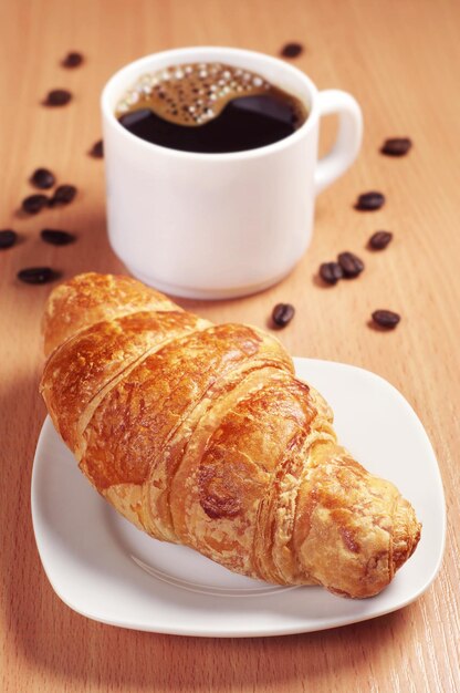 Frisches Croissant mit heißem Kaffee auf dem Schreibtisch