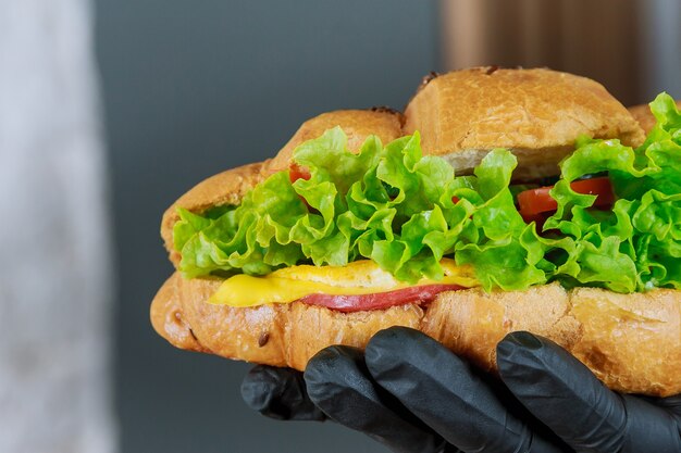 Frisches Croissant mit Schinken und Salat in der Hand eines Kellners im schwarzen Handschuh