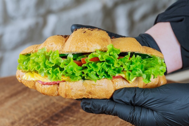 Frisches Croissant mit Schinken und Salat in der Hand eines Kellners im schwarzen Handschuh