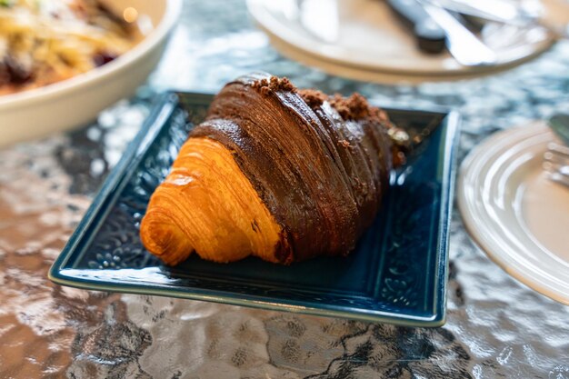 Frisches Croissant mit Schokolade gefüllt auf Keramikplatte in der Bäckerei