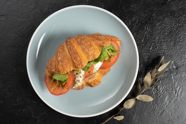 Frisches Croissant mit Tomaten, Salat und Mozzarella. Ein klassisches Frühstück aus Gebäck, Gemüse und Käse