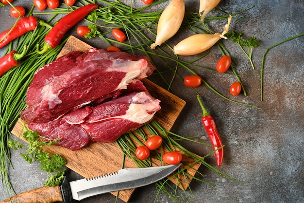 Frisches dunkles Fleisch mit Bestandteilen für das Kochen auf braunem hölzernem Schneidebrett.