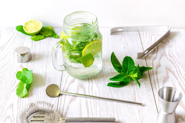 Frisches eisgekühltes Mojito-Limonade-Sommergetränk, Cocktail mit Limettenscheiben, hellgrünen Minzblättern und gefrorenen Eiswürfeln in einer transparenten Tasse, Einmachglas auf Holztisch.