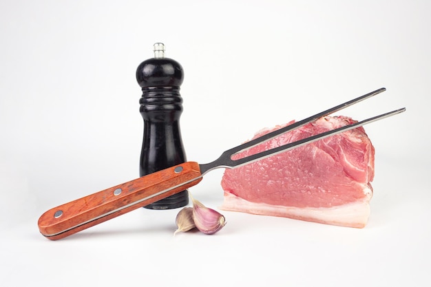 Frisches Fleisch mit Knoblauch, Pfeffer und Fleischgabel auf weißem Hintergrund Rohes Rindersteak und Gewürze zum Kochen Rohes Schweinekotelett aus Fleisch