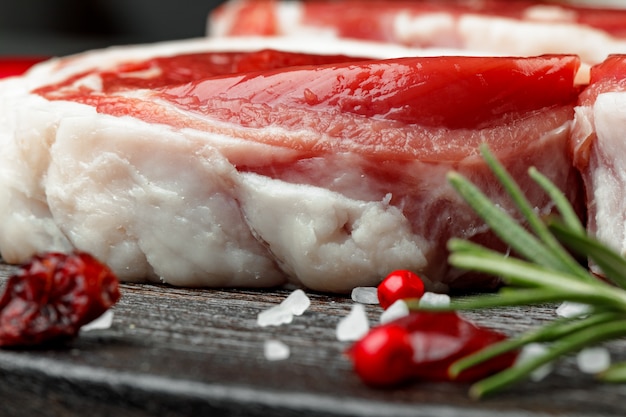 Frisches Fleisch mit Zutaten zum Kochen auf dunklem Hintergrund, Nahaufnahme