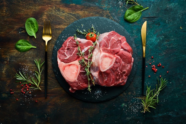 Frisches Fleisch Ossobuko-Steak am Knochen mit Rosmarin und Gewürzen Auf schwarzem Steinhintergrund Draufsicht