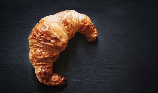 Frisches französisches Croissant auf schwarzer Steinteller-Beschaffenheitstabelle