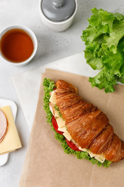 Frisches französisches Croissant mit Käse-Tomaten-Salat auf Bastelpapier am Morgen mit einer Tasse Tee