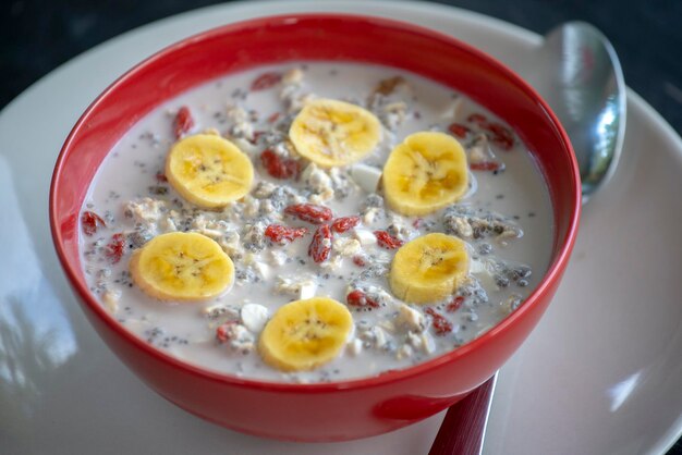 Frisches Frühstück mit Granola-Joghurt-Nüssen, Goji-Beeren, Chia-Samen und Bananen-Müsli mit Früchten und Beeren in roter Schüssel