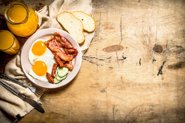 frisches Frühstück. Orangensaft mit Spiegeleiern, Speck und Brotscheiben. Auf einem Holztisch.