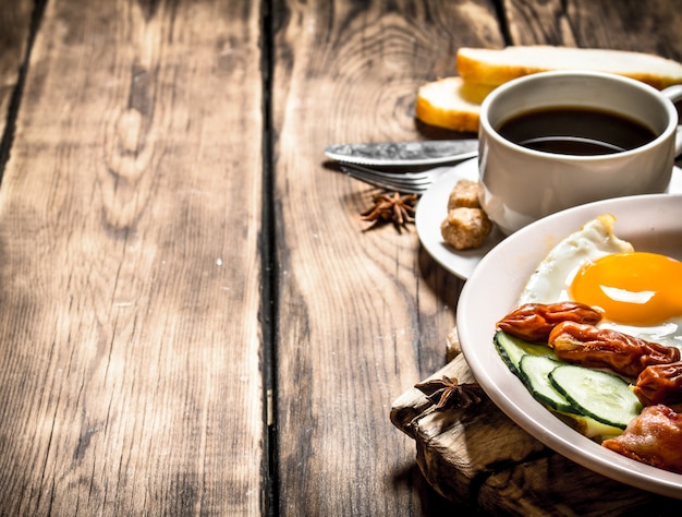 Frisches Frühstück. Tasse Kaffee, gebratener Speck mit Eiern und geräucherter Wurst. auf hölzernem Hintergrund.