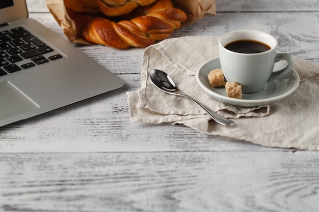 Frisches Gebäck und Tasse gebrühten Kaffee auf Tisch im Büro mit Laptop