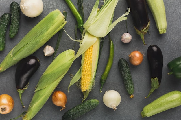 Frisches Gemüse auf grauem Hintergrund Mais Zucchini Aubergine grüne Chili Gurke und Zwiebel auf rustikalem Tisch mit Draufsicht Bio-Kochzutaten