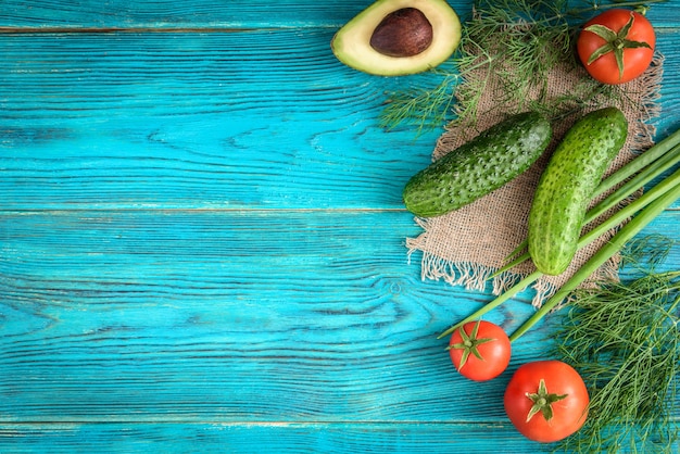 Frisches Gemüse, Holzbrett und Messer auf blauem Hintergrund. Tomaten, Gurken, Avocado, Dill und Frühlingszwiebeln. Platz für Text.