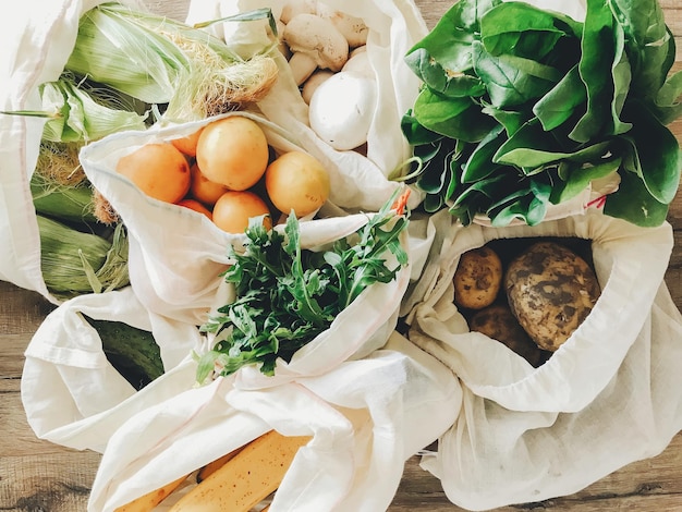 Foto frisches gemüse in öko-baumwollbeuteln auf dem tisch in der küche salat mais kartoffeln aprikosen bananen rucola pilze vom markt zero waste shopping konzept verbieten plastik