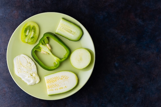 Frisches gemüse und obst auf einem grünen teller. verschiedene gemüsesorten an einer dunklen wand. paprika, tomaten, gurke, kohl, zucchini und apfel für veganer. draufsicht. speicherplatz kopieren